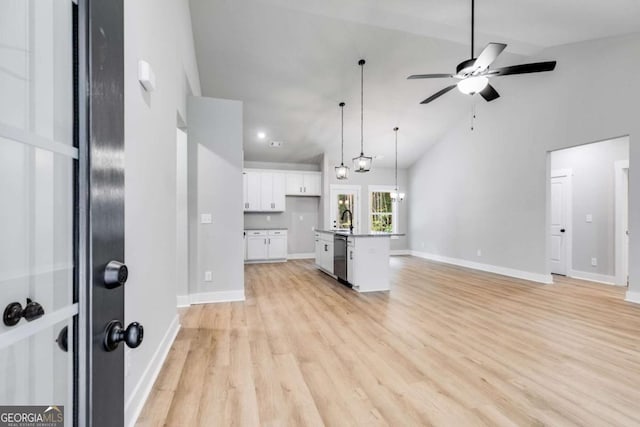 kitchen featuring a sink, white cabinetry, open floor plan, an island with sink, and decorative light fixtures