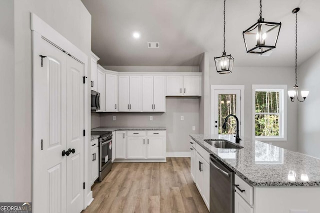 kitchen with hanging light fixtures, appliances with stainless steel finishes, white cabinets, a sink, and an island with sink