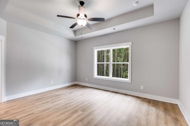 unfurnished room with a ceiling fan, a raised ceiling, light wood-style flooring, and baseboards