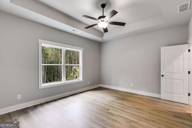 unfurnished room with a tray ceiling, light wood-style floors, visible vents, and baseboards