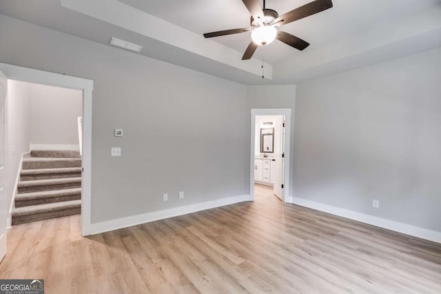 spare room with light wood-style floors, baseboards, and a tray ceiling