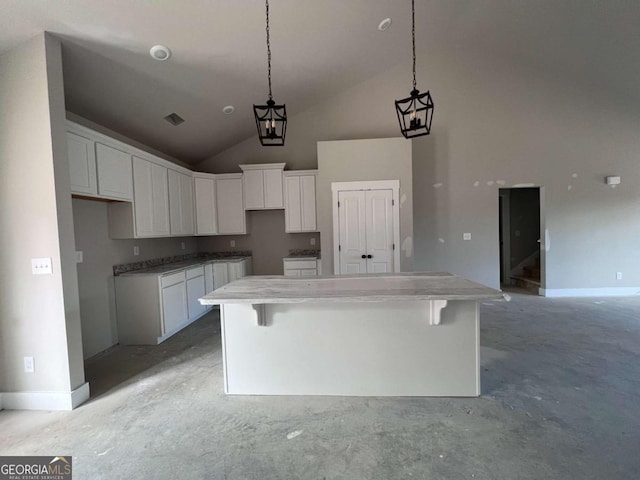 kitchen featuring white cabinets, unfinished concrete floors, a breakfast bar, decorative light fixtures, and a center island