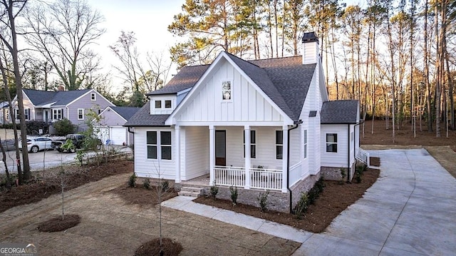 view of front of home featuring a porch, a shingled roof, concrete driveway, board and batten siding, and a chimney