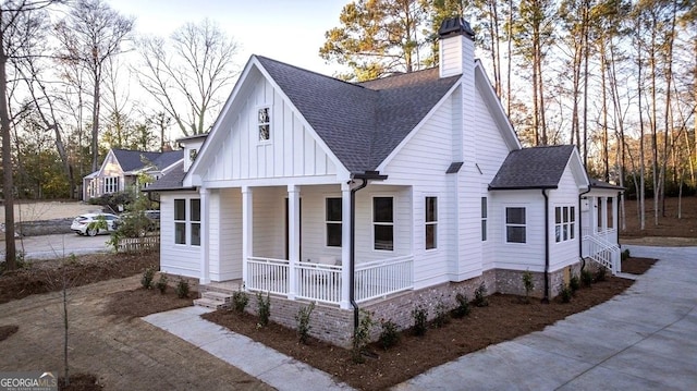 view of front of property with a porch, a shingled roof, a chimney, and board and batten siding