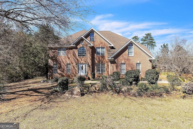 view of front of property with roof with shingles, brick siding, and a front lawn