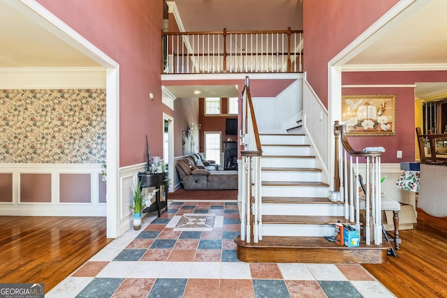 stairway with ornamental molding, wainscoting, a high ceiling, and wood finished floors