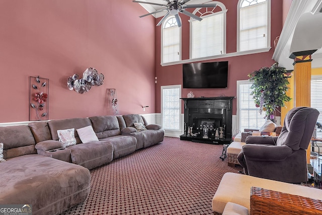 carpeted living area featuring a towering ceiling, ceiling fan, and a fireplace with raised hearth