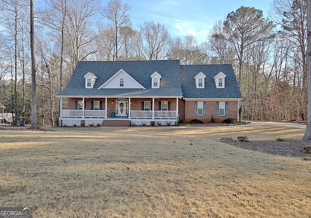 cape cod house with covered porch, roof with shingles, brick siding, and a front yard