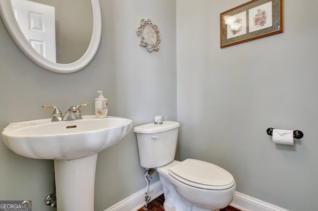 half bathroom featuring wood finished floors, toilet, and baseboards