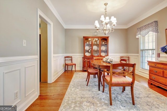 dining area with a wainscoted wall, light wood-style flooring, a chandelier, and crown molding