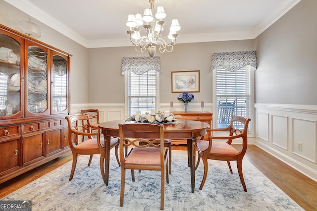 dining space with light wood finished floors, a chandelier, ornamental molding, and wainscoting