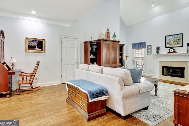 living room with a fireplace, ornamental molding, high vaulted ceiling, light wood-type flooring, and baseboards