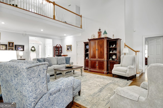 living room with a towering ceiling, ornamental molding, and wood finished floors