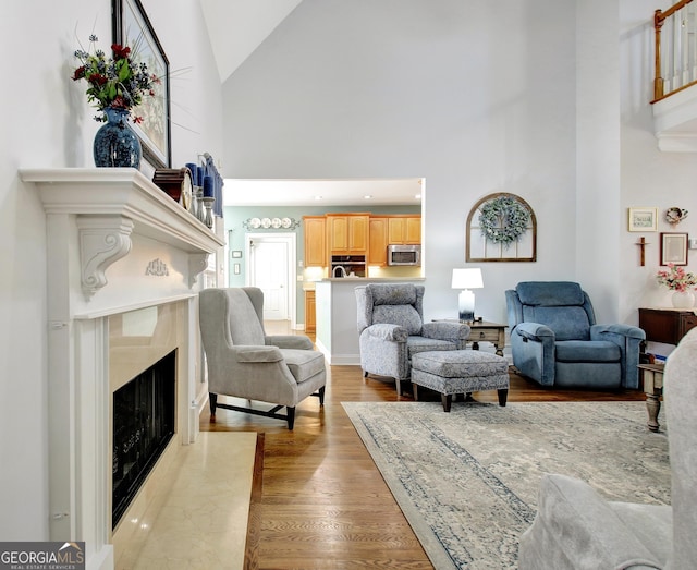 living room featuring light wood-style flooring, high vaulted ceiling, and a high end fireplace