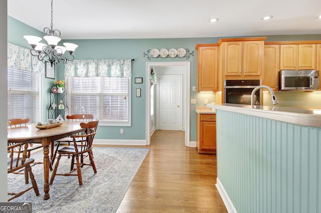 kitchen featuring stainless steel appliances, light wood-style floors, light countertops, decorative light fixtures, and an inviting chandelier