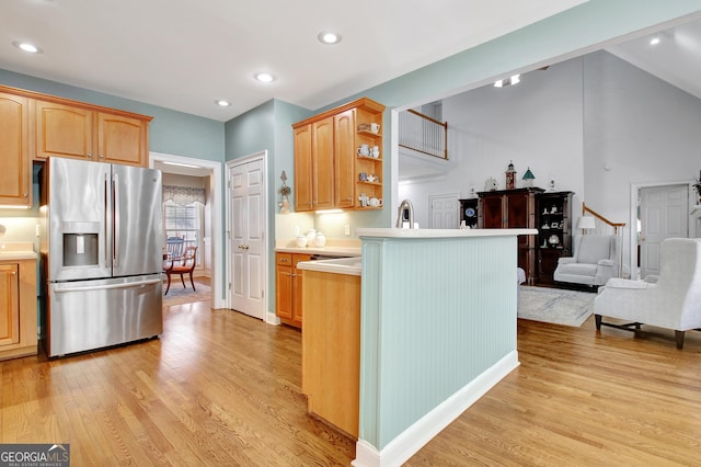 kitchen featuring light wood finished floors, open shelves, light countertops, stainless steel fridge, and a peninsula