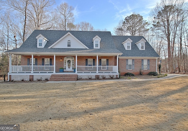 view of front of property with covered porch, a shingled roof, a front lawn, and brick siding