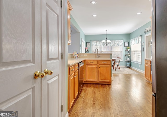 kitchen featuring decorative light fixtures, a peninsula, light countertops, light wood-style floors, and a sink