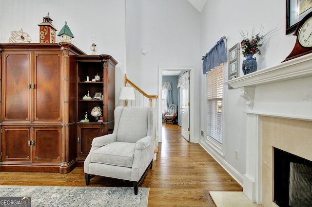 living area featuring a fireplace with flush hearth, a high ceiling, light wood-style floors, and baseboards