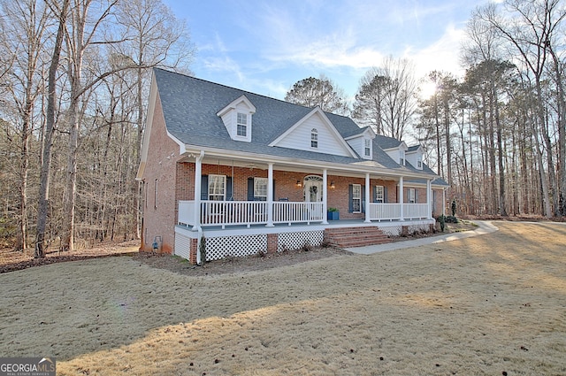 view of front of home featuring a shingled roof, a front yard, covered porch, and brick siding