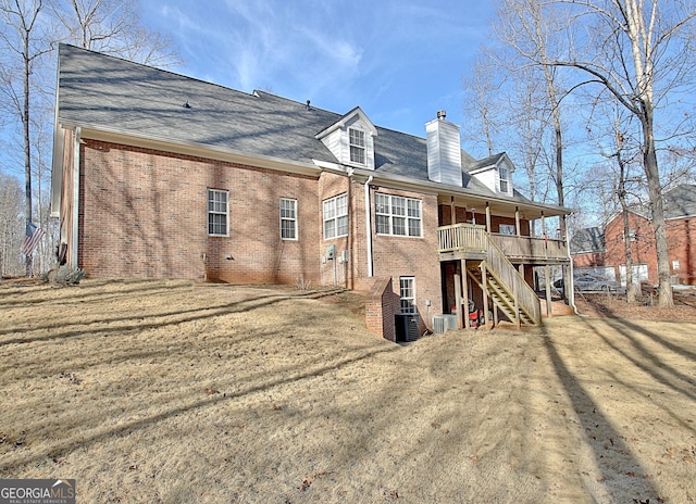 rear view of house featuring brick siding, a lawn, a chimney, and stairs