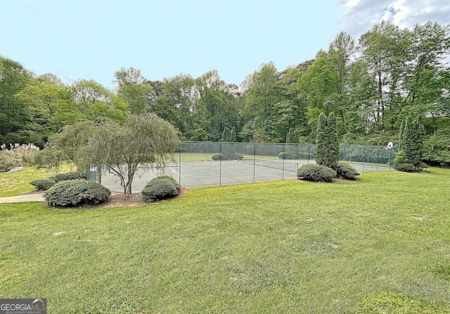 view of tennis court with fence and a lawn