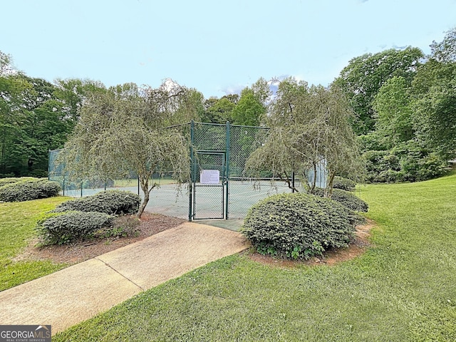 view of tennis court featuring a gate, a lawn, and fence