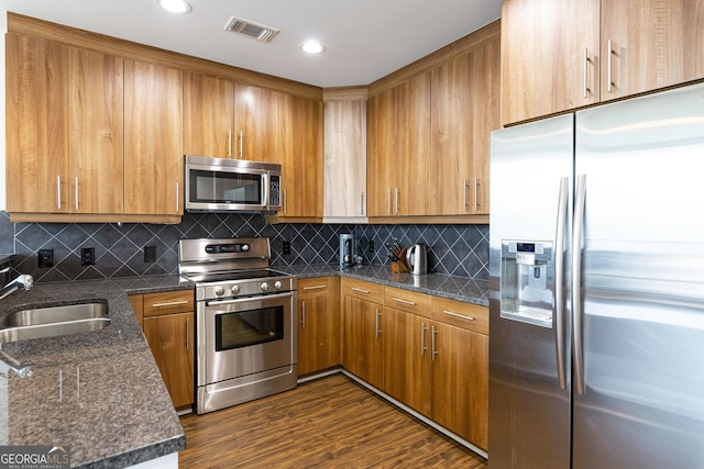 kitchen with visible vents, brown cabinets, dark wood-type flooring, stainless steel appliances, and a sink