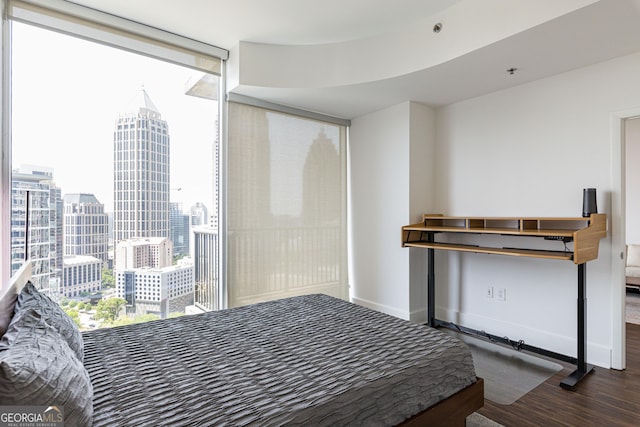 bedroom with a view of city, a wall of windows, dark wood finished floors, and baseboards