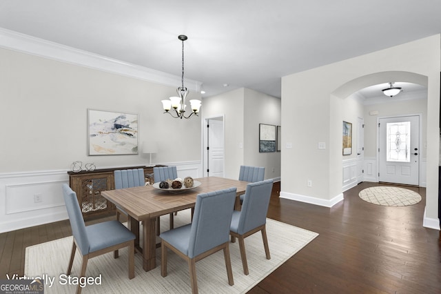 dining room featuring a notable chandelier, arched walkways, dark wood-type flooring, and ornamental molding