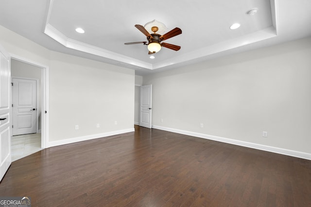 spare room featuring a raised ceiling, baseboards, and wood finished floors