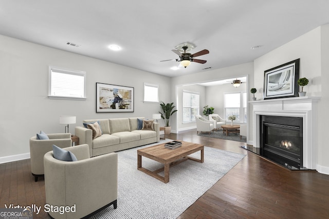 living room with baseboards, visible vents, dark wood-type flooring, and a glass covered fireplace