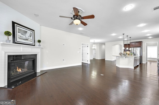 unfurnished living room featuring dark wood-type flooring, a glass covered fireplace, a ceiling fan, and baseboards