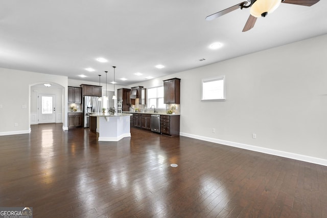 unfurnished living room featuring arched walkways, dark wood-style flooring, and baseboards