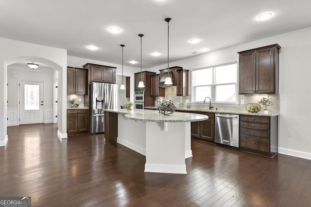 kitchen with arched walkways, appliances with stainless steel finishes, dark wood-type flooring, and dark brown cabinetry