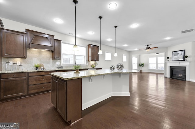 kitchen with dark wood finished floors, custom range hood, visible vents, a kitchen island, and a kitchen breakfast bar