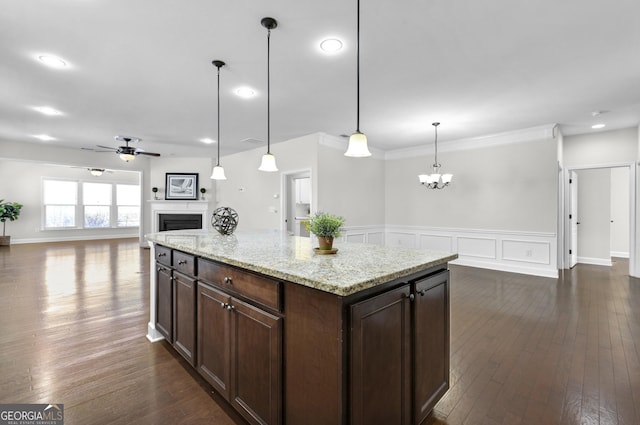 kitchen featuring ceiling fan with notable chandelier, a fireplace, open floor plan, dark brown cabinets, and dark wood-style floors