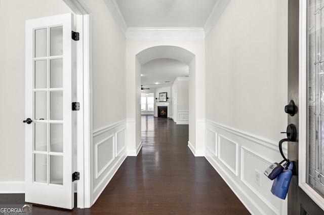 hallway with arched walkways, a decorative wall, a wainscoted wall, dark wood-style flooring, and crown molding