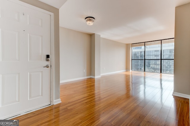 empty room with a wall of windows, light wood-style flooring, and baseboards