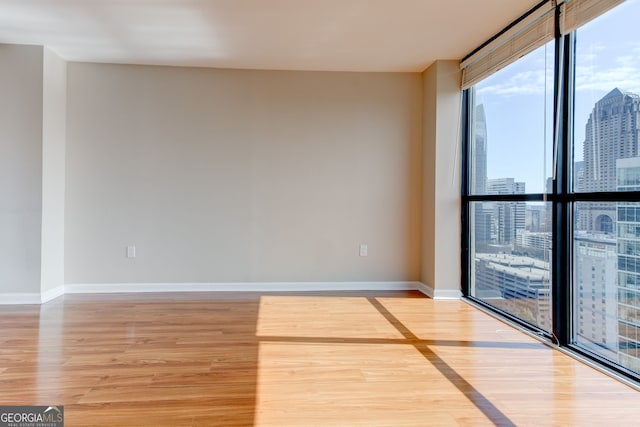 spare room with baseboards, floor to ceiling windows, wood finished floors, and a city view