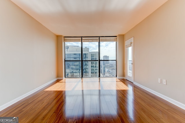 empty room with light wood-type flooring, baseboards, a wall of windows, and a city view