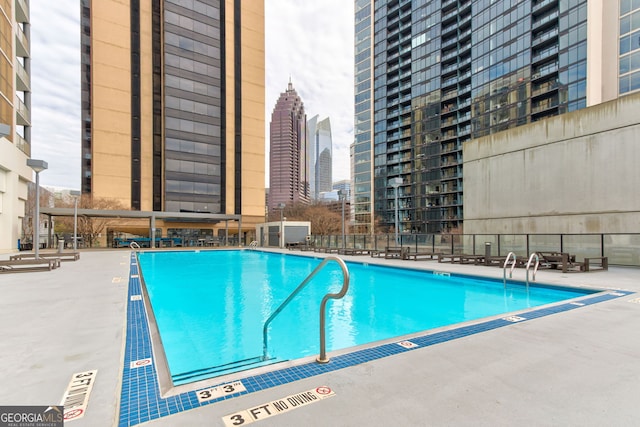 pool with a patio area, a view of city, and fence