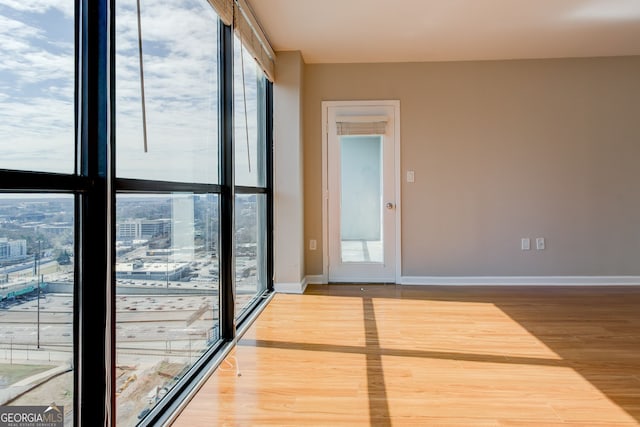 interior space featuring baseboards, a view of city, floor to ceiling windows, and wood finished floors