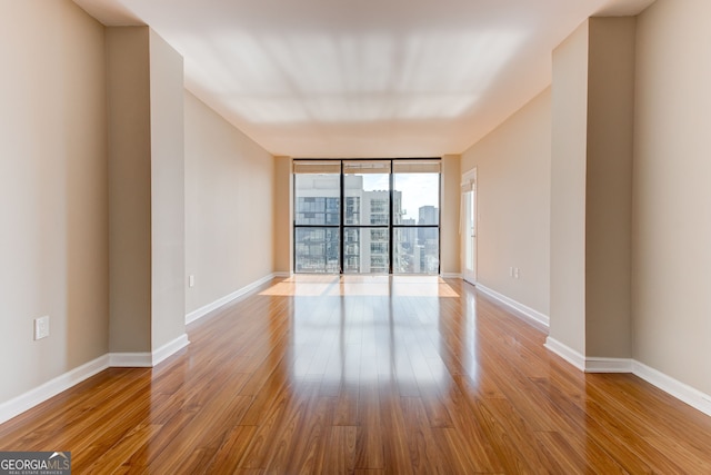 empty room with expansive windows, light wood-style floors, a view of city, and baseboards