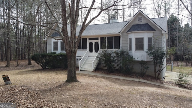 view of front of property featuring a shingled roof, stairway, a sunroom, and a chimney