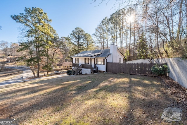 view of front of home with a chimney, fence, solar panels, and a front yard