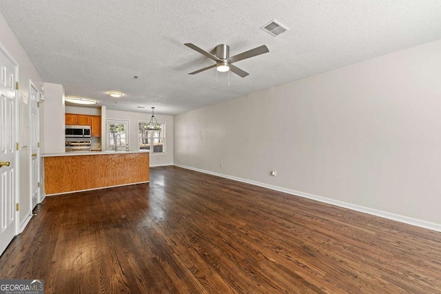 unfurnished living room with a textured ceiling, ceiling fan with notable chandelier, dark wood-type flooring, visible vents, and baseboards