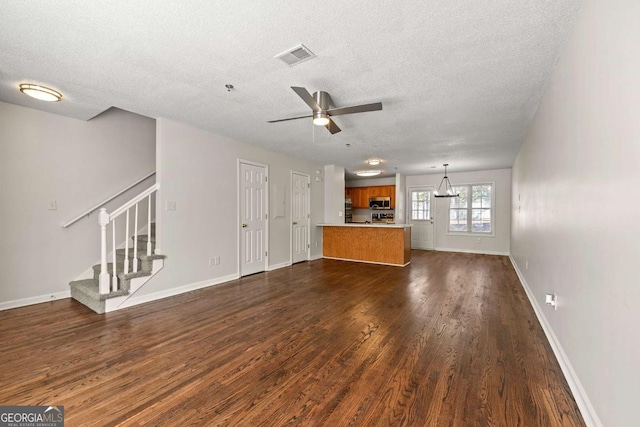 unfurnished living room with visible vents, stairway, dark wood-type flooring, a ceiling fan, and baseboards