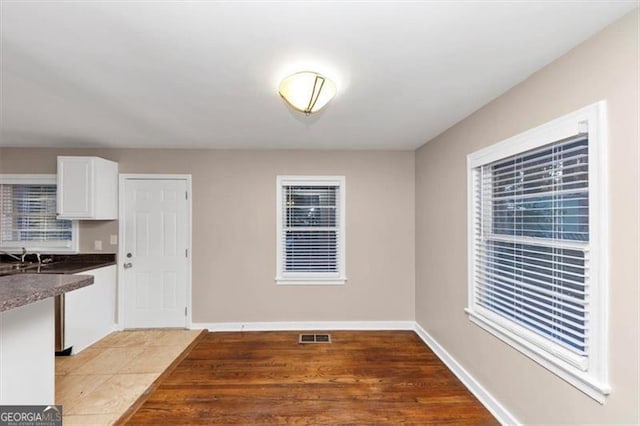 unfurnished dining area with visible vents, a sink, baseboards, and wood finished floors