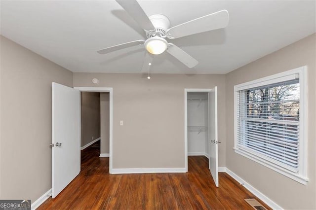 unfurnished bedroom featuring dark wood-style flooring, visible vents, baseboards, a closet, and a walk in closet